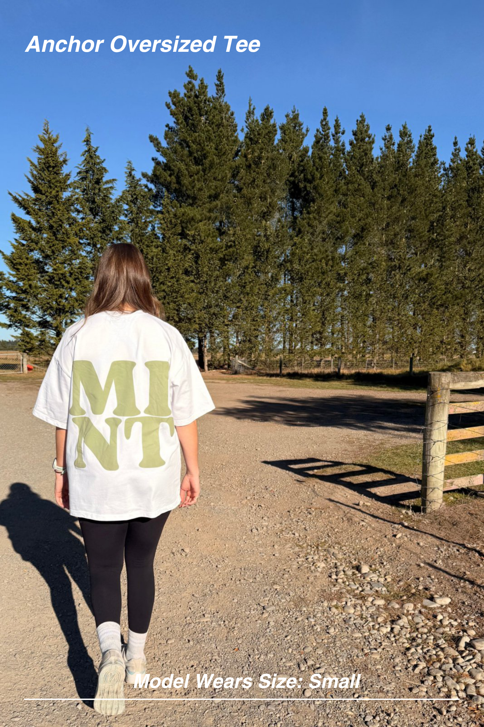 Mint Activewear Anchor Oversized Tee in white, full back view on a gravel path showing the longline oversized drop shoulder.
