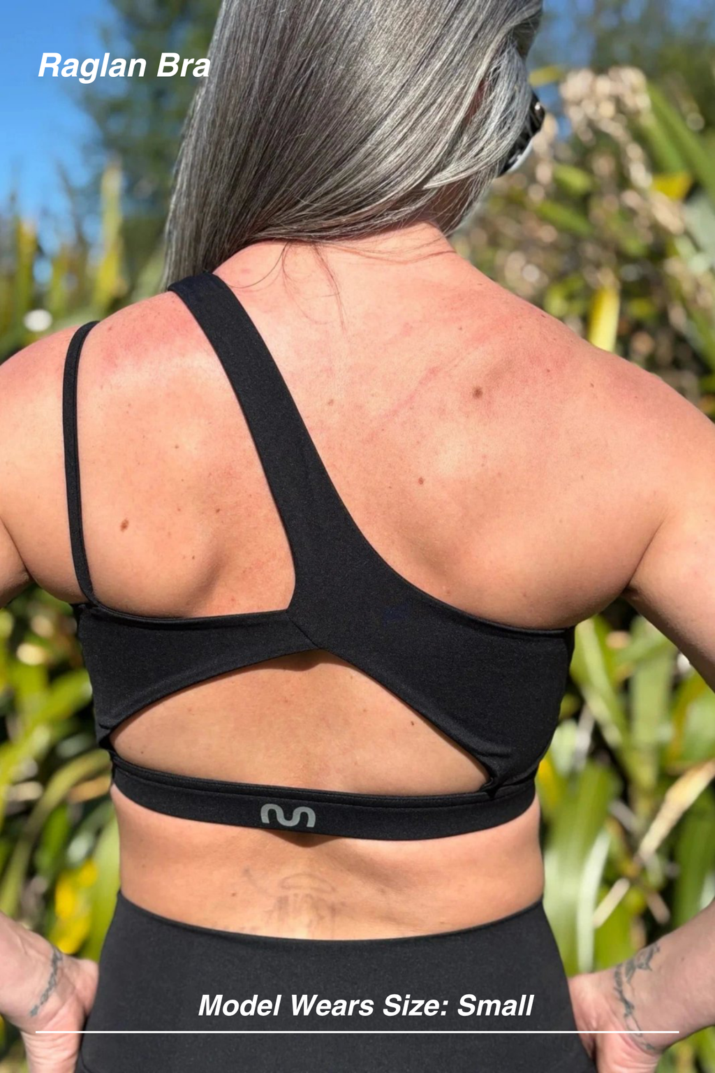 Mint Activewear Raglan Bra in Black, outdoor back view with the asymmetric strap and open cut-out band.