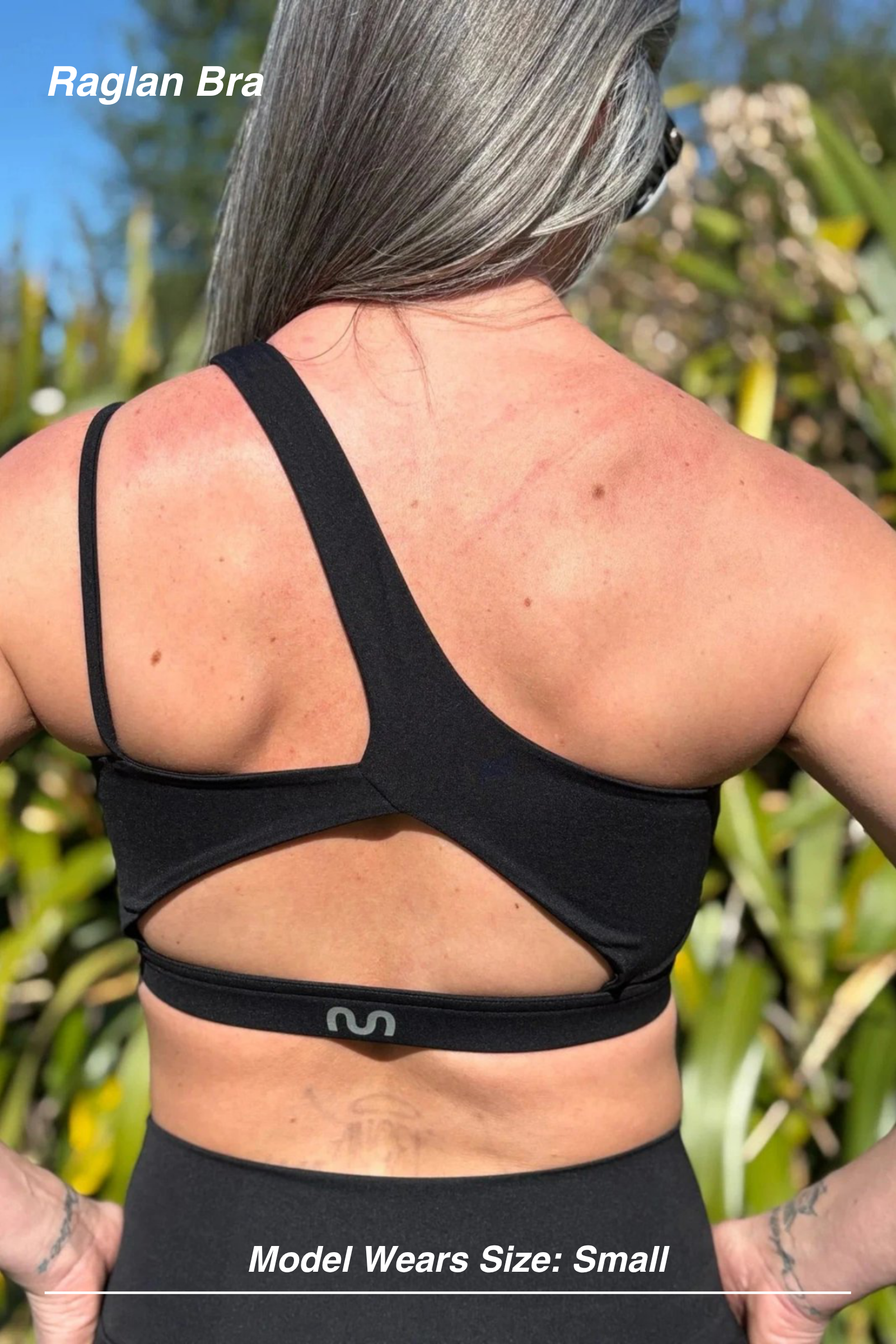 Mint Activewear Raglan Bra in Black, outdoor back view with the asymmetric strap and open cut-out band.