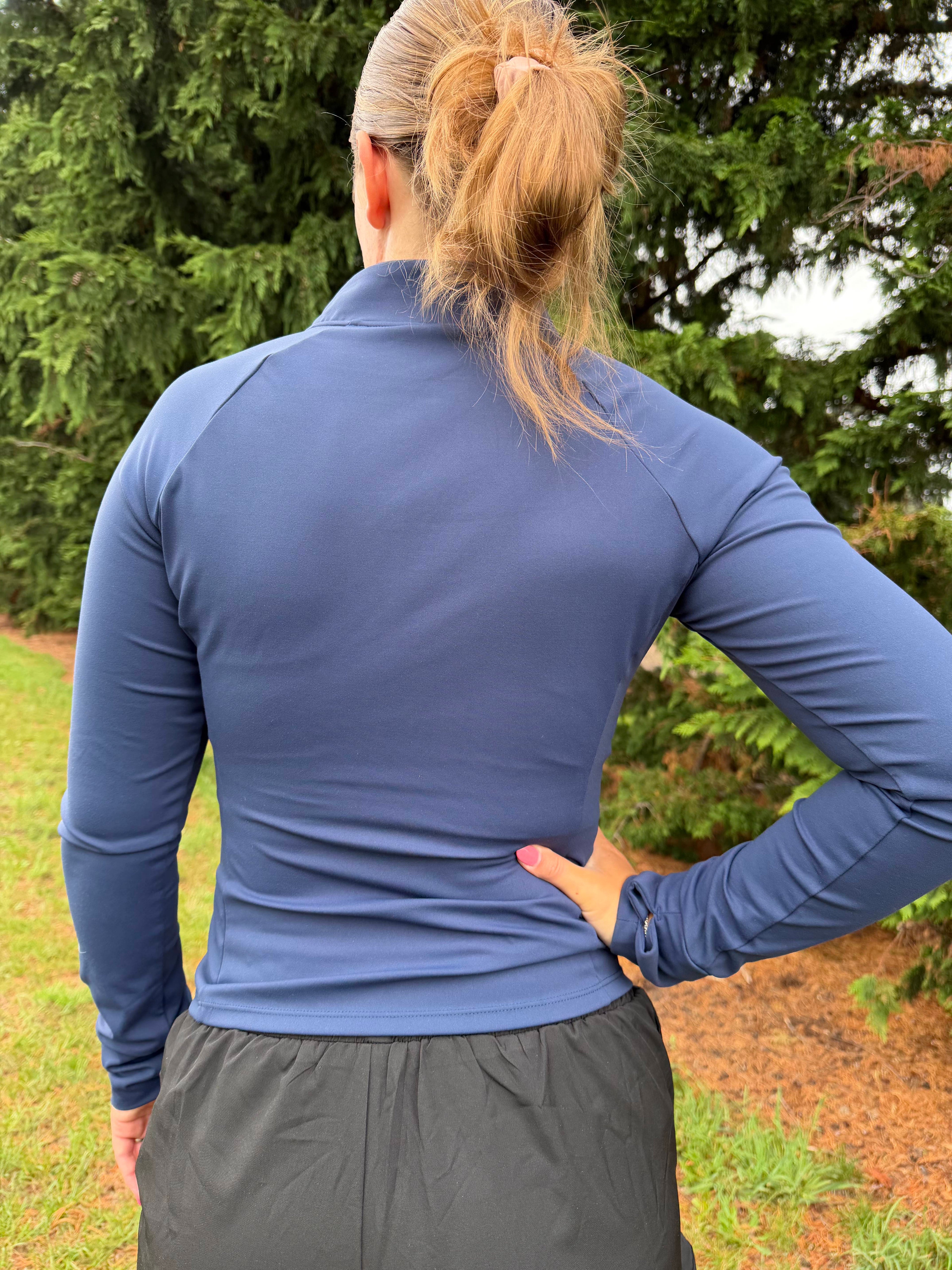 Women wearing a blue long-sleeve shirt and gray shorts outdoors with greenery in the background