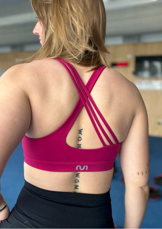 Person wearing a pink sports bra with visible tattoos on a blurred indoor background